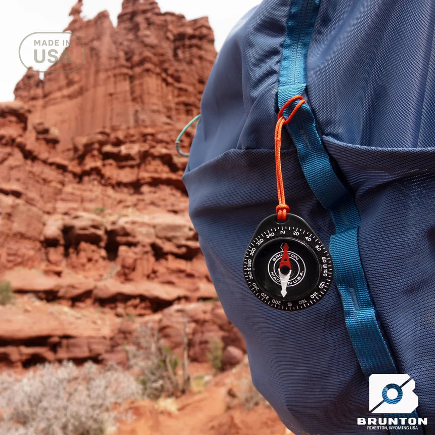 Blue backpack with a Brunton compass attached, set against a desert landscape.