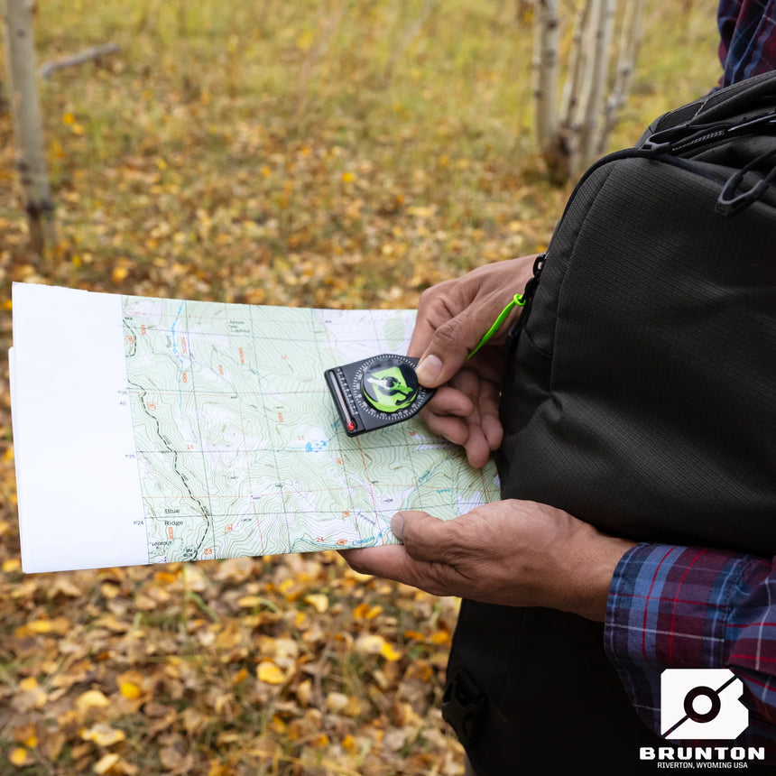 Person holding a map and compass outdoors with Brunton logo visible