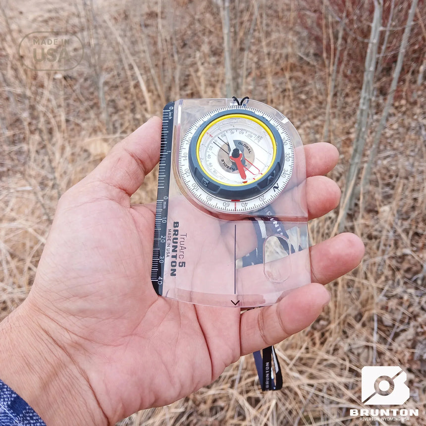 Hand holding a Brunton compass against a natural background