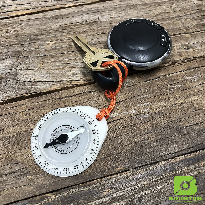 Keychain compass with a key on an orange cord, placed on a wooden surface with Brunton logo.
