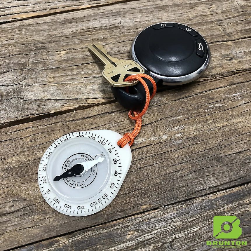 Keychain compass with a key on an orange cord, placed on a wooden surface with Brunton logo.