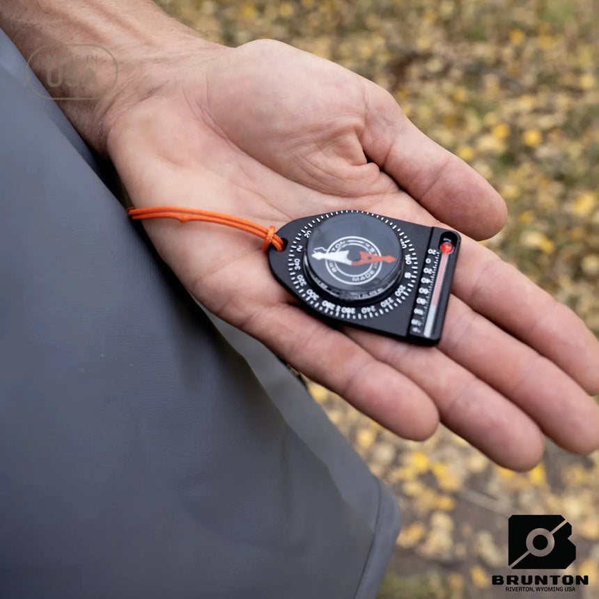 Person holding a Brunton compass on a blurred natural background