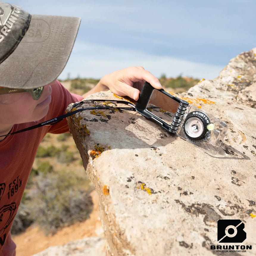 Person using a Brunton tool on a rock with a clear sky background