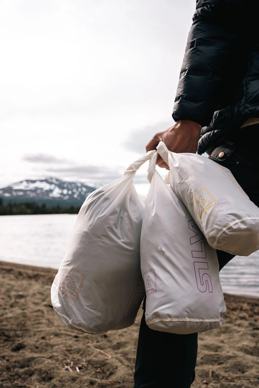 Person holding two white bags with visible branding near a body of water.