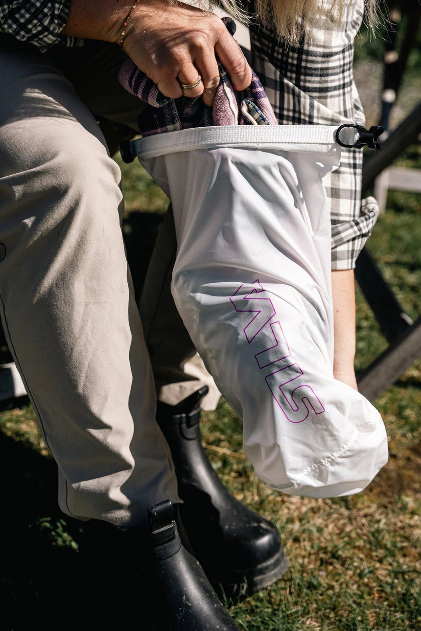 Person holding a white mesh bag with pink text, wearing plaid shorts and black boots, outdoors.