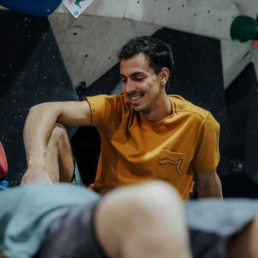 Wild Country Climbing Session Men's T-Shirt Joshua Brown - Model Sitting Down With Climbing Wall Background