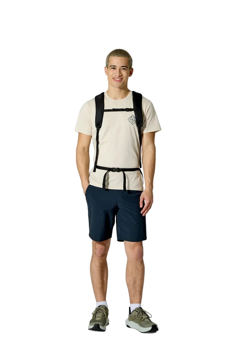 Man wearing a beige t-shirt, navy shorts, and a black backpack on a white background