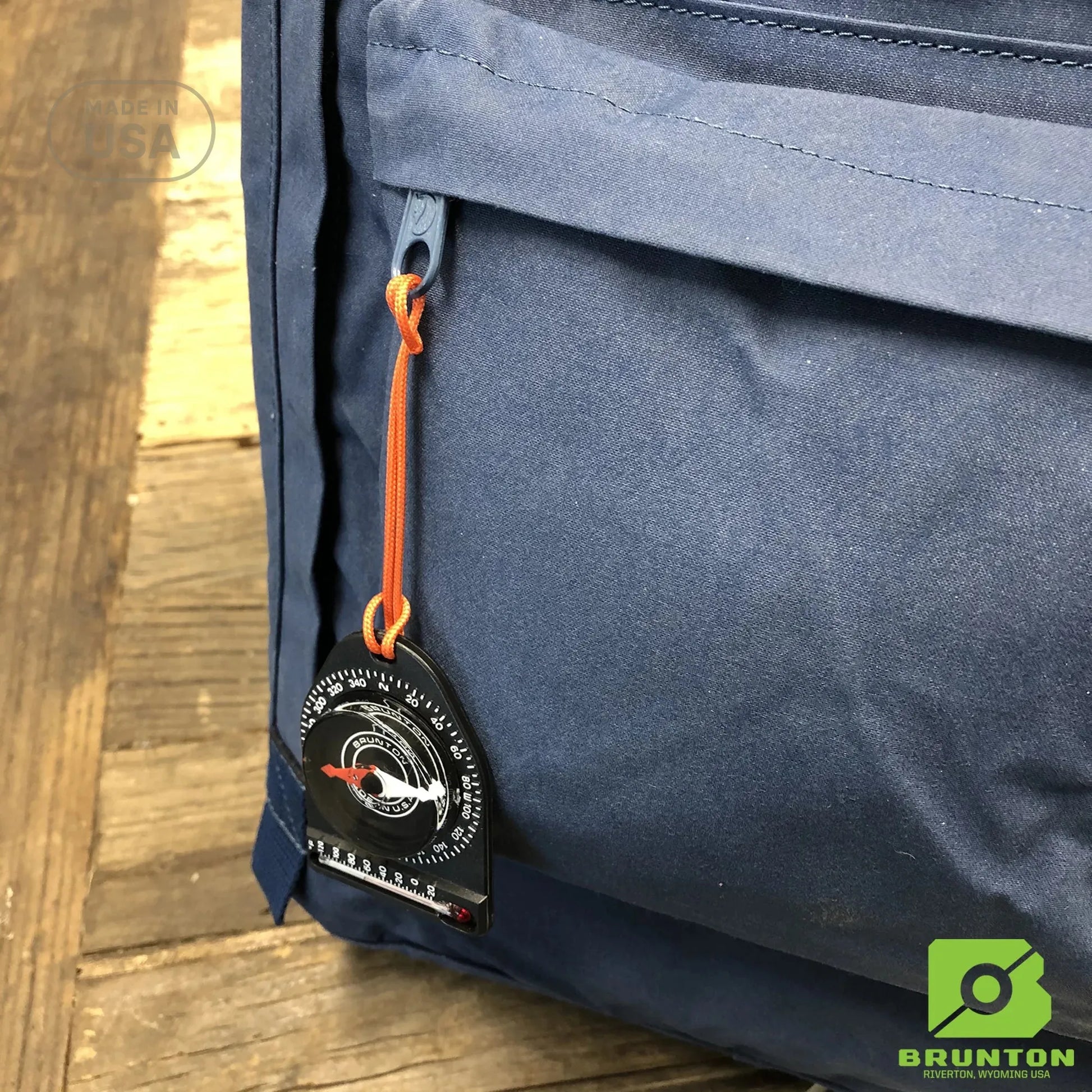 Blue backpack with a Brunton compass attached on a wooden surface