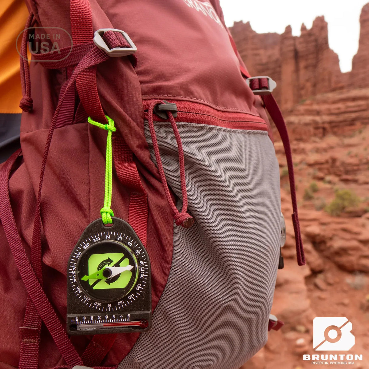 Person wearing a red backpack with a Brunton compass attached, set against a desert landscape.