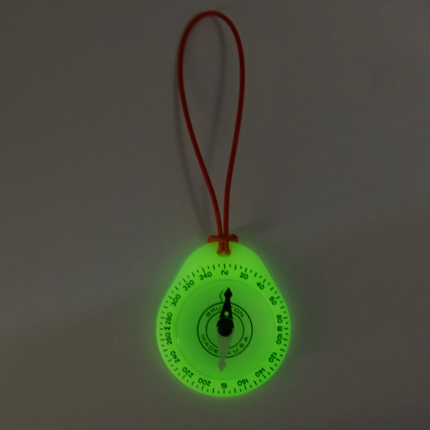 Glowing green compass with a red string on a dark background