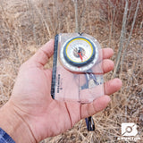 Hand holding a Brunton compass against a natural background