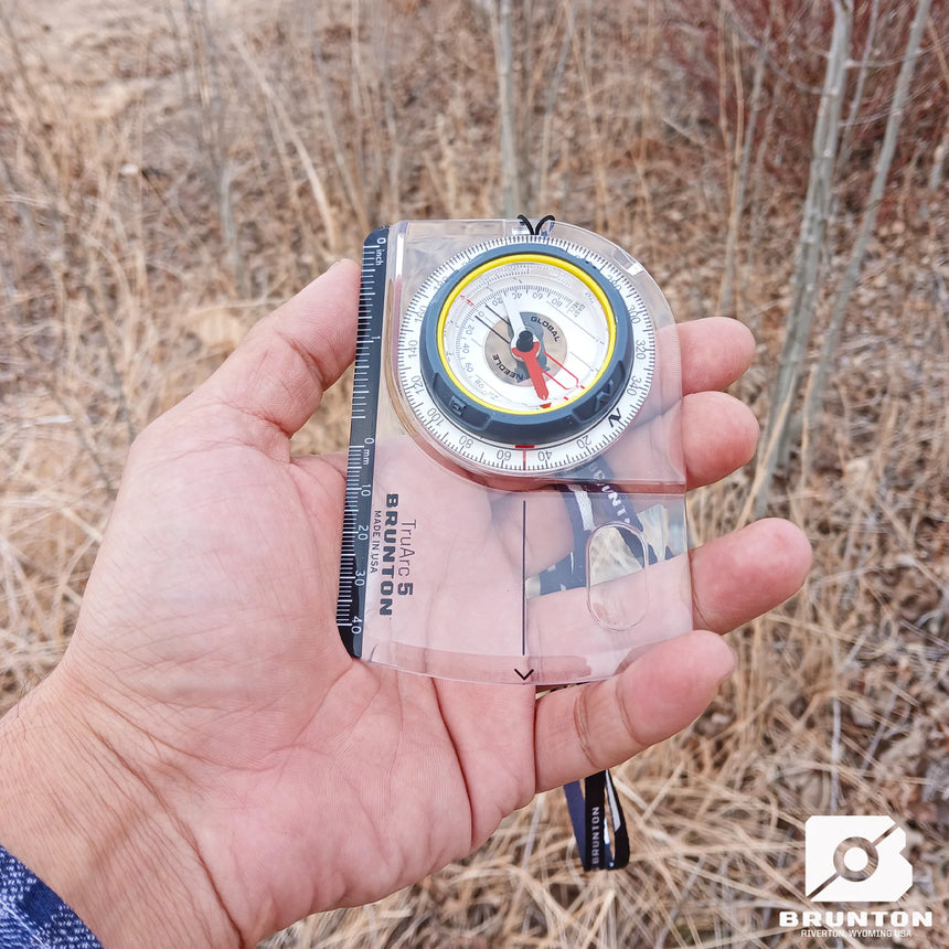 Hand holding a Brunton compass against a natural background