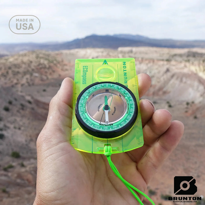 Hand holding a Brunton compass with a desert landscape in the background