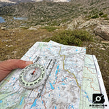 Map and compass held over a topographic map with a mountainous landscape in the background