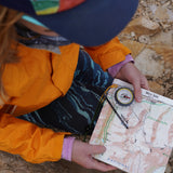 Person in orange jacket holding a map with a compass on a rocky surface